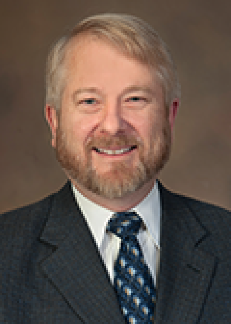 Man with blonde hair, beard, smiling, black jacket, white shirt and blue tie